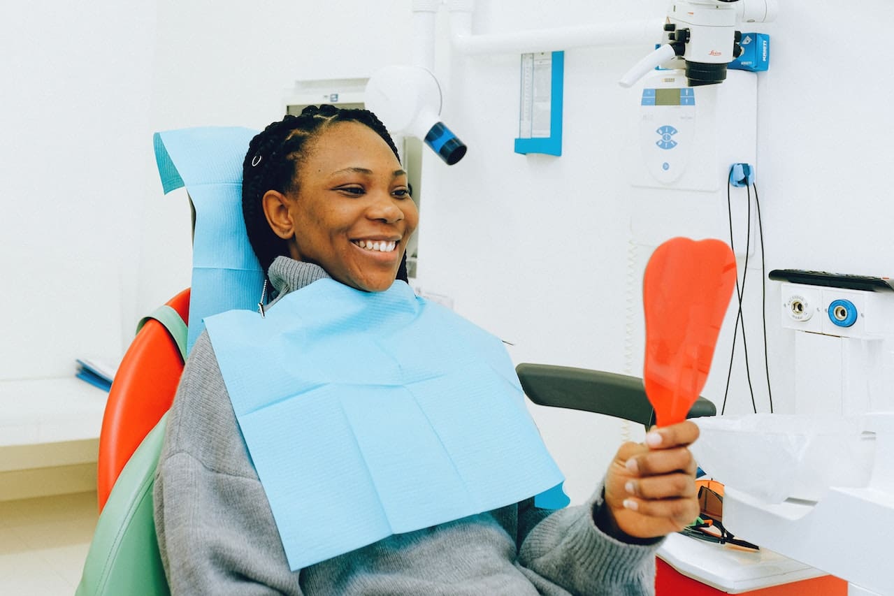 Woman smiling while looking at mirror sitting on the dental chair