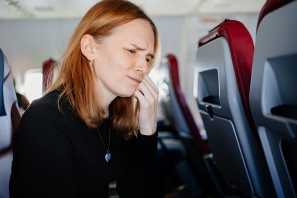 Patient on a plane with dental emergency holding their cheek