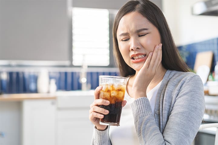 A woman holding a cold soda and her cheek while cringing in pain