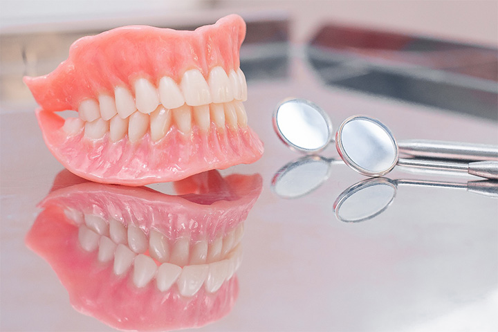 A closeup of two dentures sitting on a glass countertop.