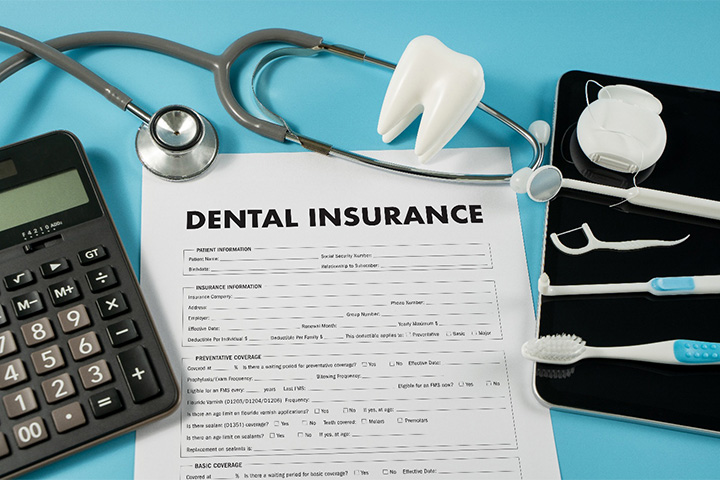 A dental insurance form next to a calculator and some dental tools.