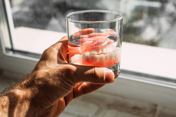 A man holding a glass of water containing some dentures.