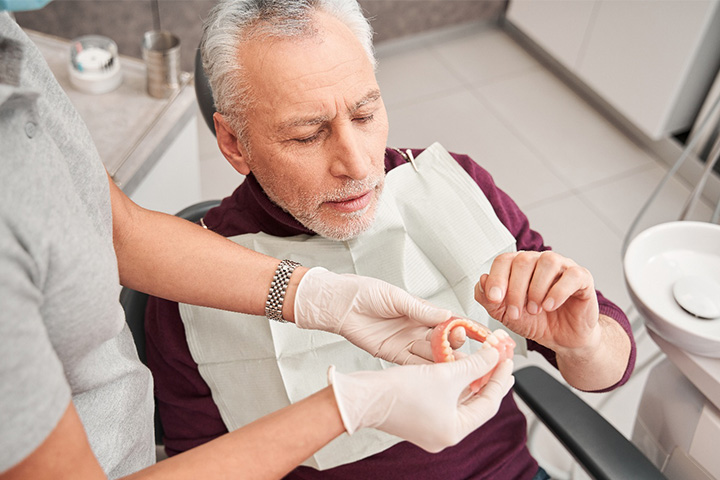 A patient looking closely at dentures held by a dentist.