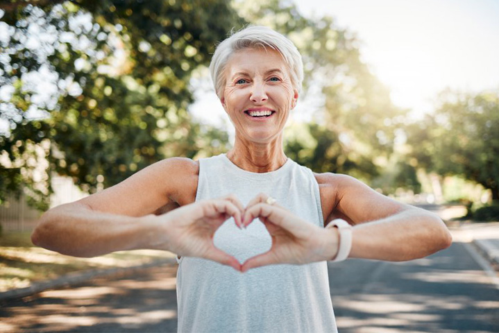 Lady smiles while making shape of heart with her hands.