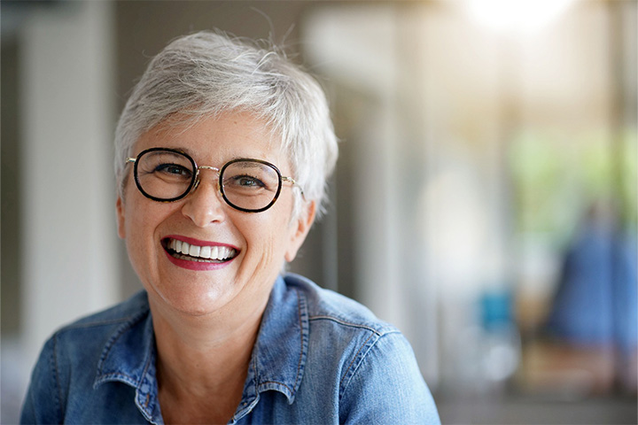 Woman wearing black rimmed glasses and smiling with dentures.