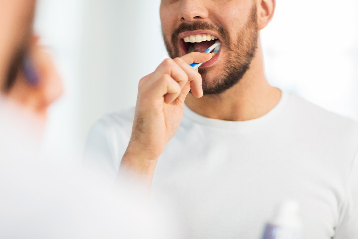 Man in white shirt brushing his teeth.