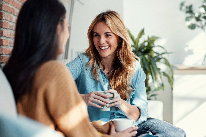 Two friends smiling while enjoying cup of coffee together.