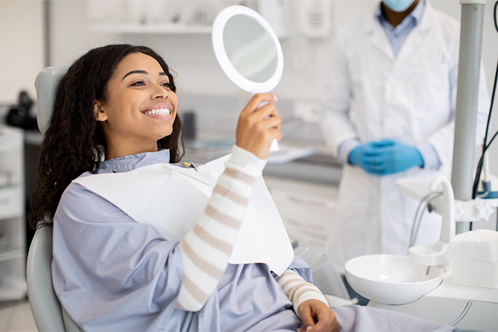 Woman smiling while looking at reflection in handheld mirror.