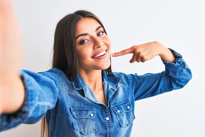 A dental patient smiling and pointing to her teeth.