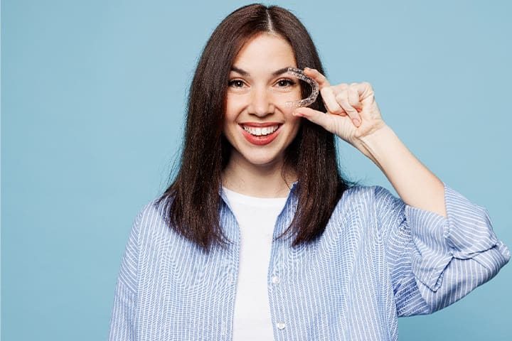 A patient smiling and holding their Invisalign aligner.