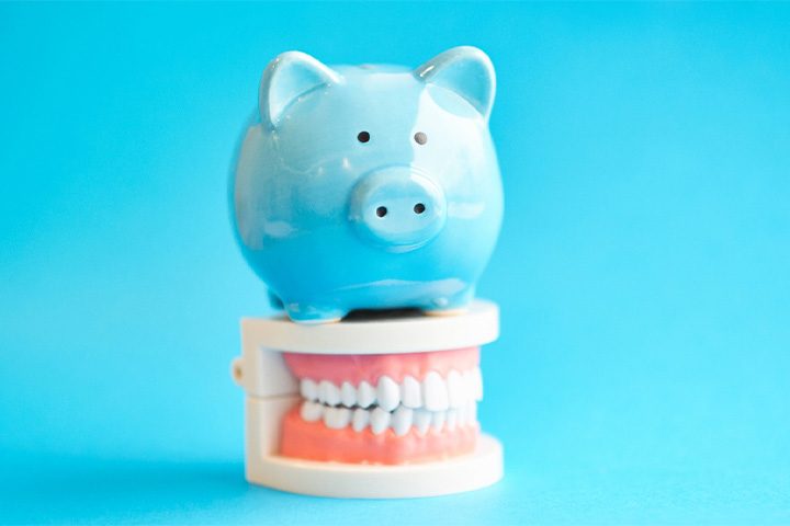 A piggy bank sitting on top of a model denture against a blue background.