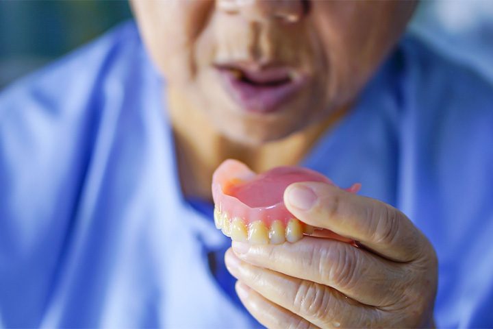 Older man holding his dentures in Danvers.