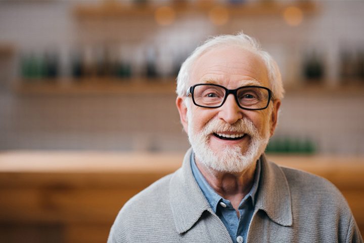 Senior man with glasses smiling in kitchen.