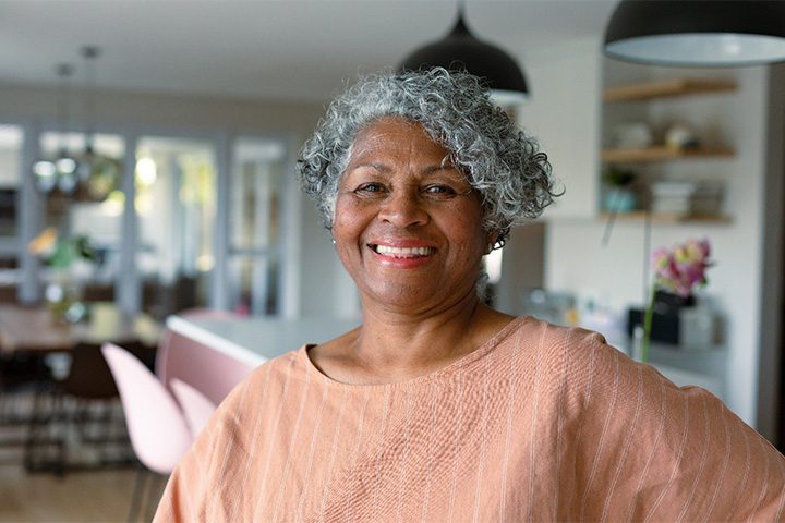 Senior woman smiling at home with peach-colored shirt.