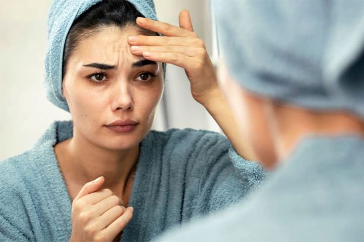 Woman looking in mirror, concerned about signs of aging