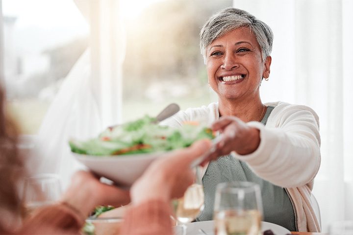 Woman smiling and passing a salad and enjoying the benefits of dentures in Danvers.